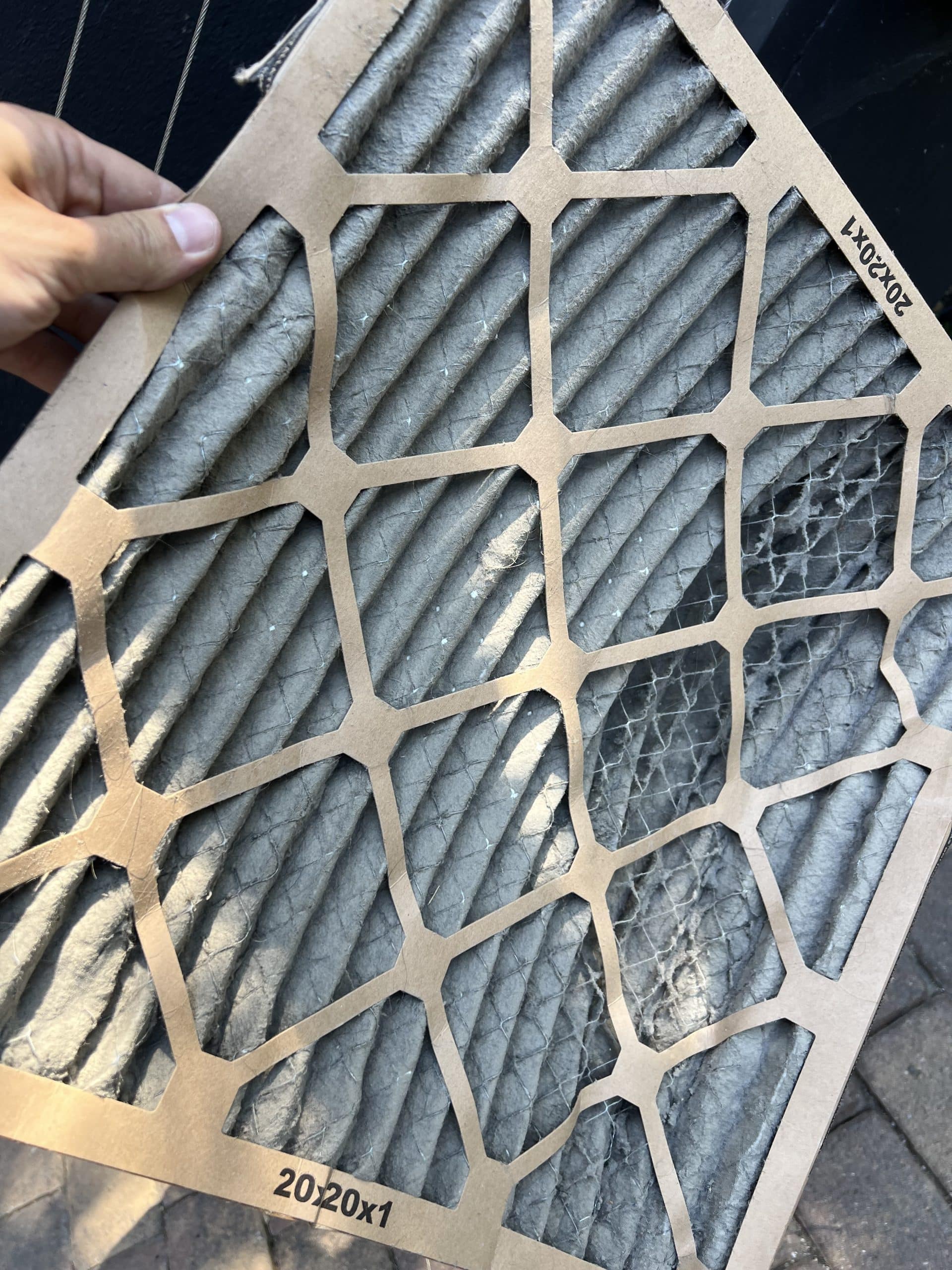 Person holds old, dusty air filter outdoors.