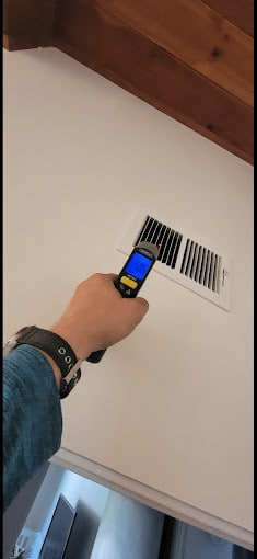 Hand using thermometer near wall vent