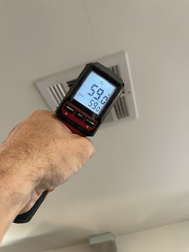 Hand holding infrared thermometer near ceiling vent.